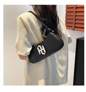 Détail d'un sac sous le bras en cuir noir avec logo argenté porté par un modèle