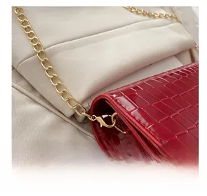 Detail shot of red crocodile texture handbag with glossy finish and gold metal hook