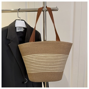 Detail of woven straw tote bag with brown stripes and canvas straps on a hanger