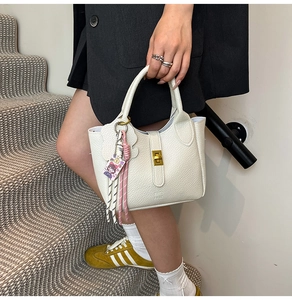Fashionable white lychee pattern leather handbag held by a model on modern stairs