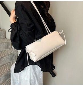 Close-up view of a minimalist cream-white underarm bag with elegant side bow knots
