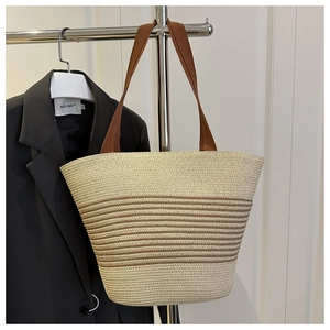 Detail of hand-woven straw tote bag with brown stripes and wide fabric handles