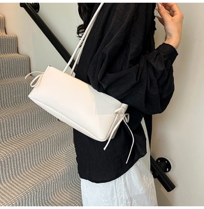 Gedetailleerde opname van een witte minimalistische okseltas met elegante zijstrikaccenten.