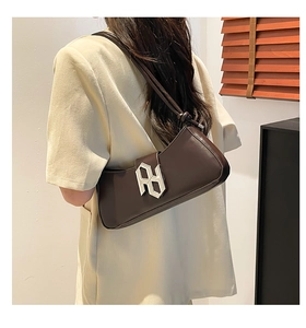 Détail d'un sac baguette marron foncé avec boucle argentée porté par un mannequin à l'épaule