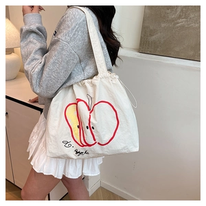 Detail shot of white canvas tote bag featuring red apple print and drawstring closure