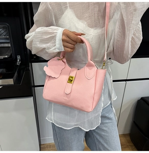 Detailed shot of a pink litchi grain leather handbag with gold lock held by a model
