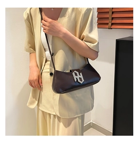 Détail du sac baguette en cuir marron foncé avec boucle argentée porté sur un tailleur