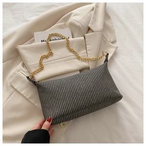 Détail d'un sac à main tissé rectangulaire à rayures grises et bandoulière chaîne dorée