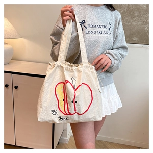 Detailed shot of white canvas tote bag featuring apple illustration and drawstring closure