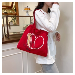 Detail of red canvas tote bag with apple embroidery and drawstring closure on shoulder