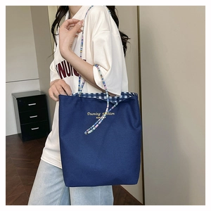 Detail of dark blue canvas tote bag featuring colorful beaded straps and plaid lining
