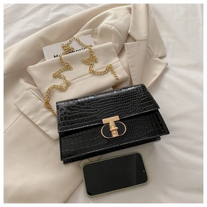 Detail of black crocodile-patterned bag with golden T-shaped lock and metal chain strap