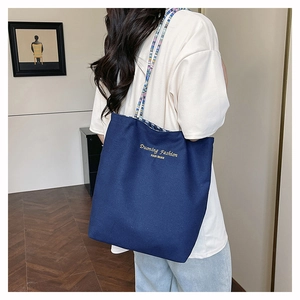Detail of navy canvas tote bag featuring colorful woven straps and gold logo print