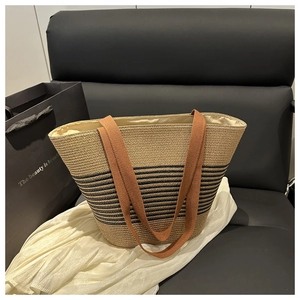 Detail of woven straw tote bag with black stripes and brown fabric handles