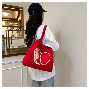 Detail of red canvas tote bag featuring white hand-drawn apple print and handle