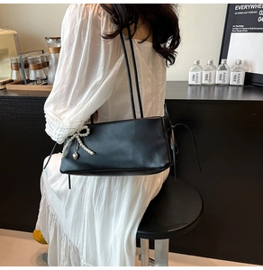 Elegant black underarm bag with pearl bow charm and heart pendant in lifestyle setting