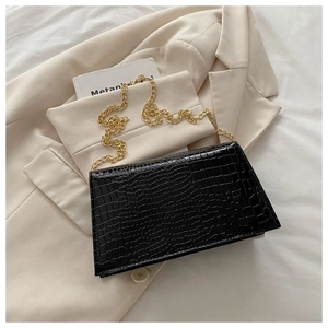 Detail of glossy black crocodile texture on flap bag with elegant gold chain strap