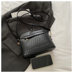 Close-up of black woven leather texture and gold hardware on stylish crossbody bag