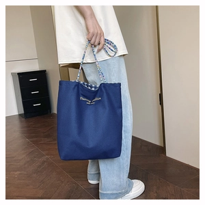 Detail of navy canvas tote bag with woven handles and checkered lining and gold lettering