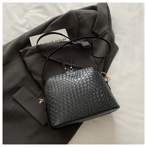 Detail of black shell-shaped crossbody bag with woven texture and gold hardware zipper