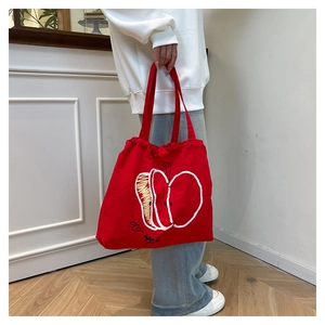 Detail of red nylon tote bag featuring a minimalist white apple print and artistic text
