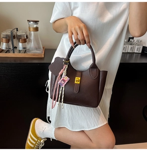 Model holding a stylish brown lychee textured bucket bag with gold clasp detail