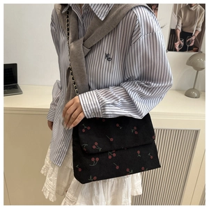 Détail du sac bandoulière en velours noir avec broderie cerise et texture de chaîne