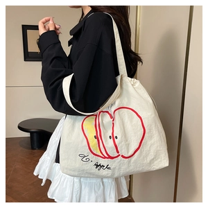Detail of a beige canvas shoulder bag featuring a cute apple print and drawstring closure