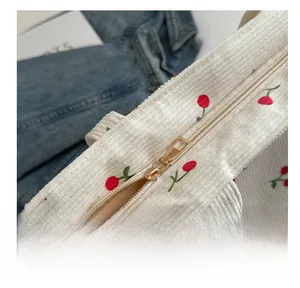Détail de la fermeture éclair dorée sur le sac cabas en velours côtelé brodé cerise
