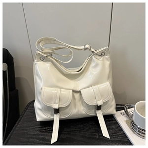 Detail of a shiny cream shoulder bag featuring utility pockets and silver hardware on a table