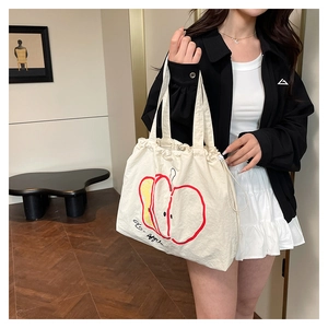 Detail view of cream nylon tote bag with red apple print and drawstring closure design