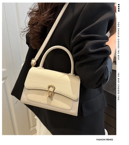 Detail of beige crossbody bag featuring woven texture flap and golden metal clasp
