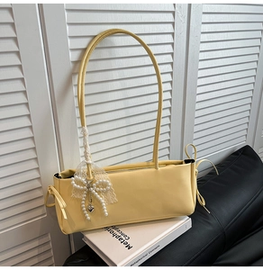 Detailed shot of a yellow minimalist underarm bag featuring a pearl bow charm decoration