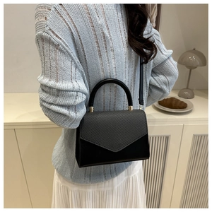 Detail of black structured handbag featuring woven flap texture and gold hardware