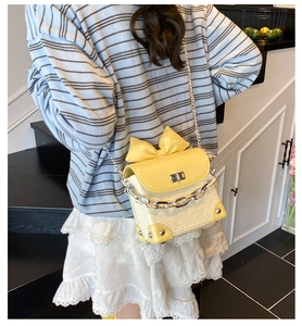 Detail of yellow bow straw crossbody bag worn by a model in a bright modern interior