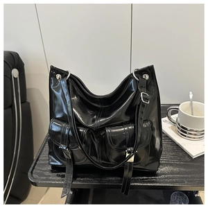 Close-up of black glossy tote bag with dual front flap pockets and silver hardware