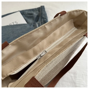 Detail of woven tote bag showing beige straw texture and brown fabric handle