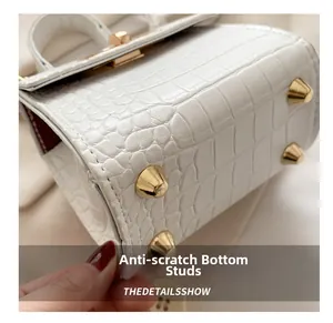 Detailed close-up of the white crocodile texture handbag base with gold protective studs