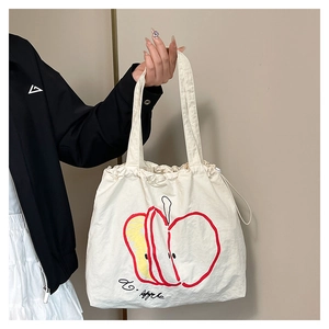 Detail of drawstring canvas tote bag featuring red and yellow apple print with Apple text