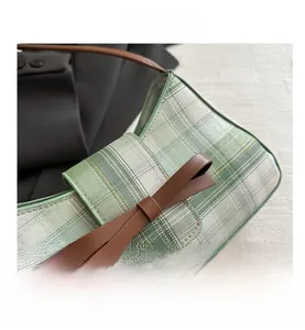 Close-up of green plaid fabric with a dark brown leather bow on an underarm bag