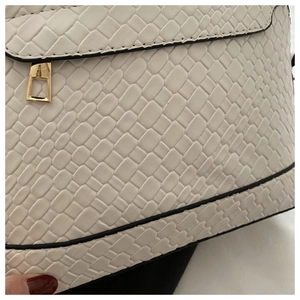 Close-up of white woven texture shoulder bag with gold zipper and black edge paint