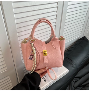 Close-up view of a pink lychee grain leather bucket bag with gold hardware and charms.