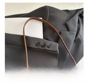 Detail shot of green and white plaid bag with brown leather strap and grey blazer jacket