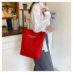 Detail of red canvas tote bag featuring colorful beaded shoulder strap and gold lettering