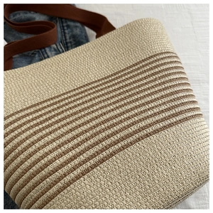Detail of woven straw tote bag with brown stripes and canvas shoulder strap texture