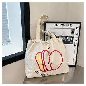 Detail of off-white canvas tote bag featuring red apple print and artistic calligraphy