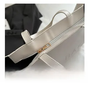 Detail of smooth light gold zipper and embossed BAG text on minimalist white tote bag