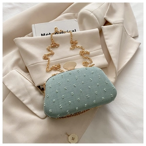 Detail of mint green textured fabric handbag with gold chain strap and metal clasp