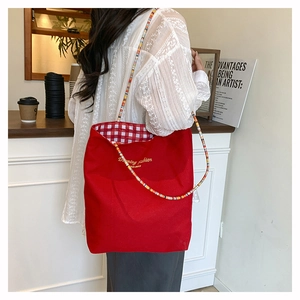 Detail of red canvas tote with plaid lining and colorful beaded strap worn by model
