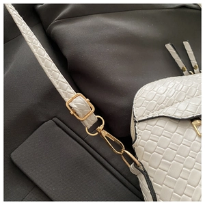 Detail of white woven texture crossbody bag with gold metal hardware on grey suit